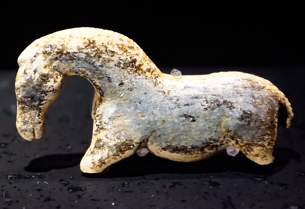 The "Wild Horse" of the Vogelherd Cave has an arched neck, a detailed head, reasonable horse proportions, and the beginning of a tail. The legs are broken off and today the ivory is speckled with black.