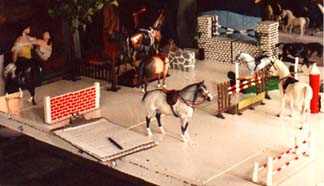 A table full of model horses wearing english tack near jumps